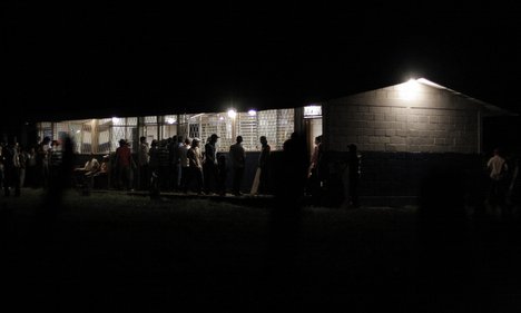Nighttime gathering at illuminated buildings in Los Calpules, Nicaragua, with people assembled outside