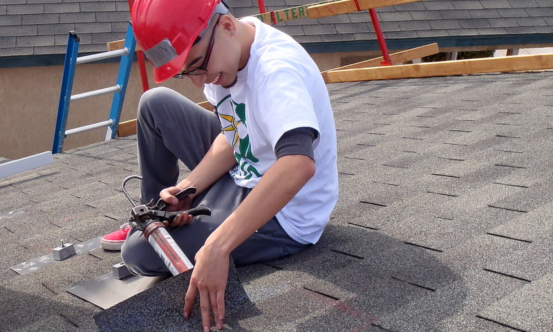 Worker in red helmet installing roofing material on flat roof during school construction project