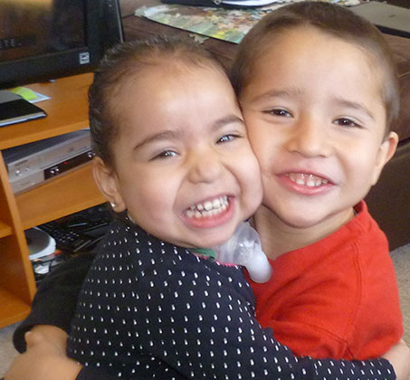Two young children smiling brightly at the camera in a home office setting