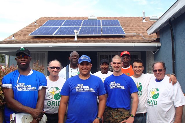 Group of volunteers in blue "The Mission Continues" shirts standing in front of house with solar panels installed on roof