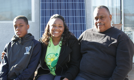 Three people smiling together outdoors with solar panels visible in background