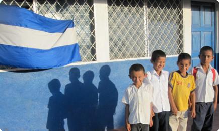 Five students standing in front of blue wall with Nicaraguan flag, announcing international program