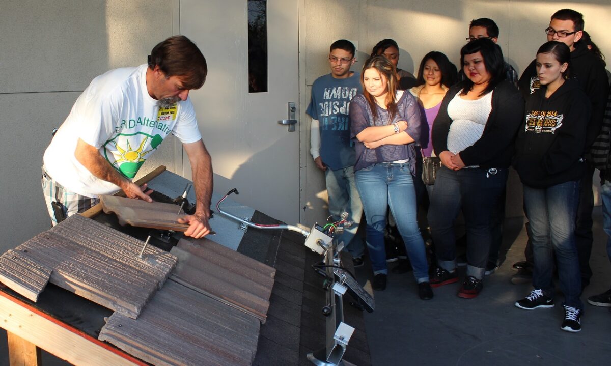 Instructor demonstrates solar panel installation to a group of students watching intently in a workshop setting