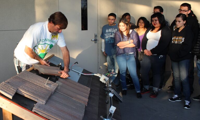Instructor demonstrates solar panel installation to a group of students watching intently in a workshop setting