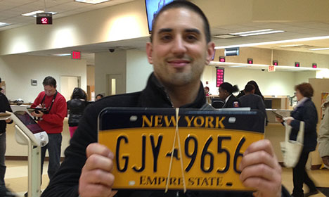 Man holding New York license plate GJY 9656 in indoor setting