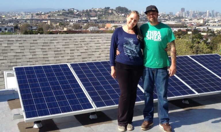 Two people stand on a rooftop with solar panels and San Francisco cityscape behind them