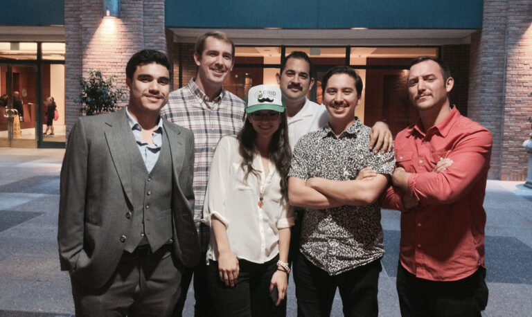 Five people posing together in a courtyard, one wearing a GRID cap, supporting Mustache March fundraiser