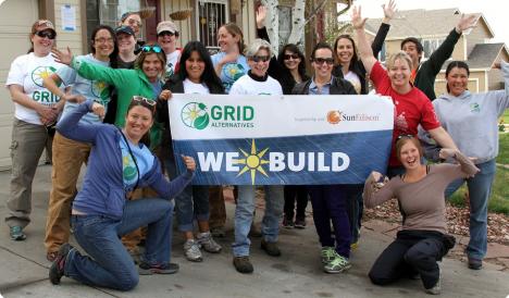 Group of people holding "GRID Alternatives" and "We Build" banners at a community event