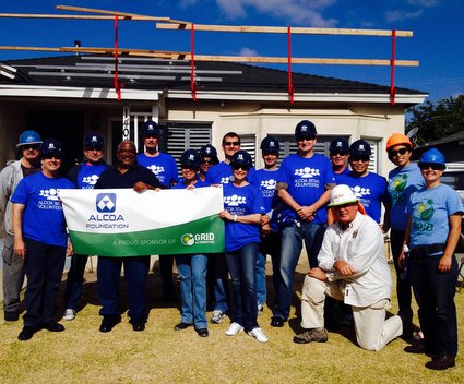 Alcoa volunteers in blue shirts holding green banner with retired veteran at construction site
