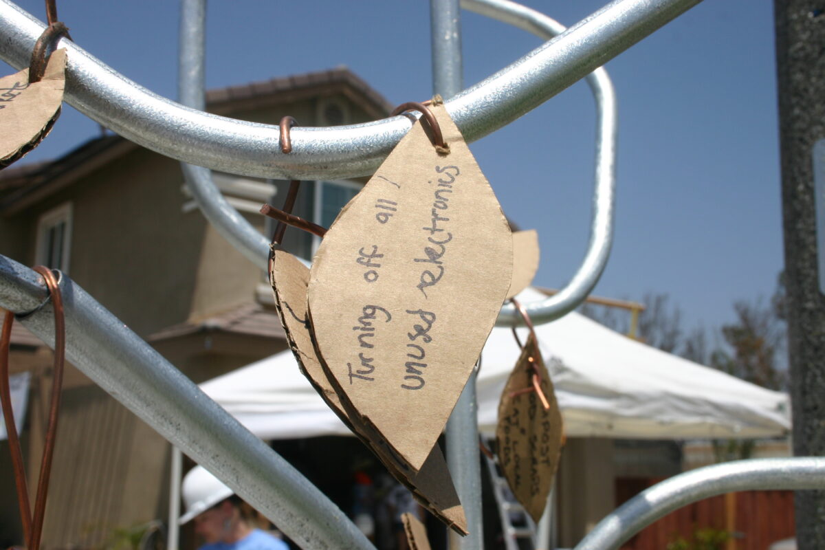 Leaf-shaped tag hanging from metal structure reading "living off the grid under solar panels