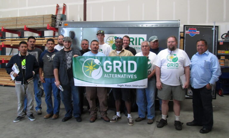 Group of workers holding GRID Alternatives banner in a warehouse facility