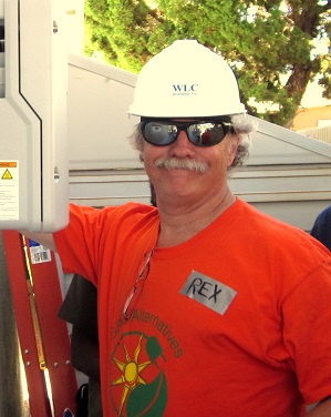 Man wearing white WLC hard hat and orange shirt with sun logo standing outdoors