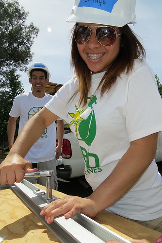 High school students in blue hard hats and green organization shirts install solar panel components outdoors