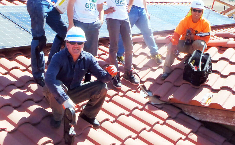 Workers installing solar panels on a red tile roof during a training demonstration