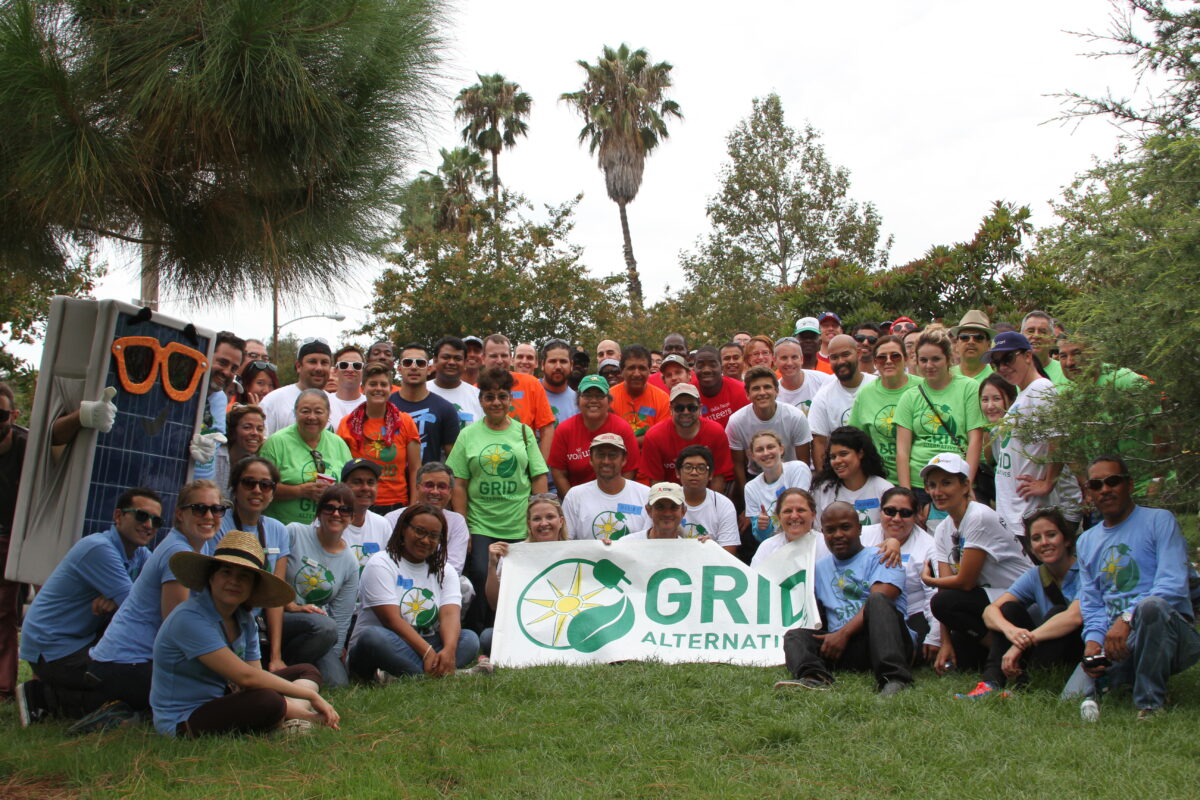 Large group holding GRID Alternatives banner at outdoor solar energy event in Orange County