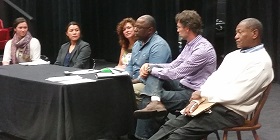 Panel discussion with six diverse speakers seated at table with microphone at eco-festival event