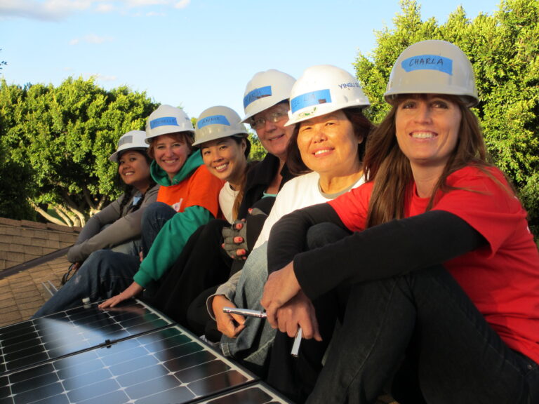 Six women in hard hats smile while posing on a solar panel installation