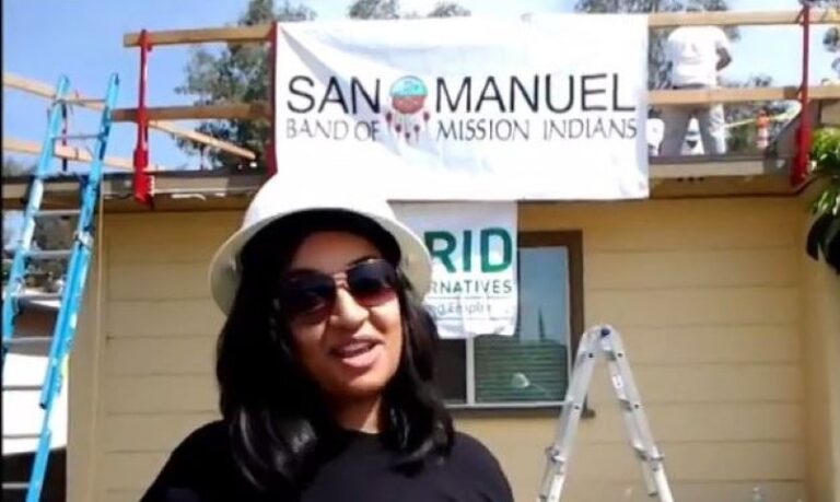 Woman in white cap and sunglasses in front of San Manuel Band of Mission Indians banner during construction work