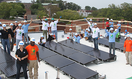 Group of people on rooftop installing solar panels during volunteer event
