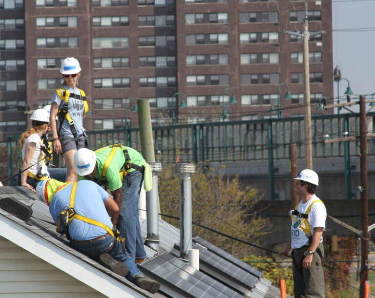 Construction workers on rooftop with safety equipment during expansion project near city buildings
