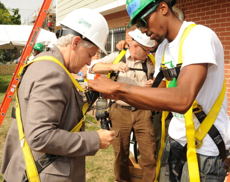 Workers in safety gear and hard hats receiving training on fall protection equipment outdoors