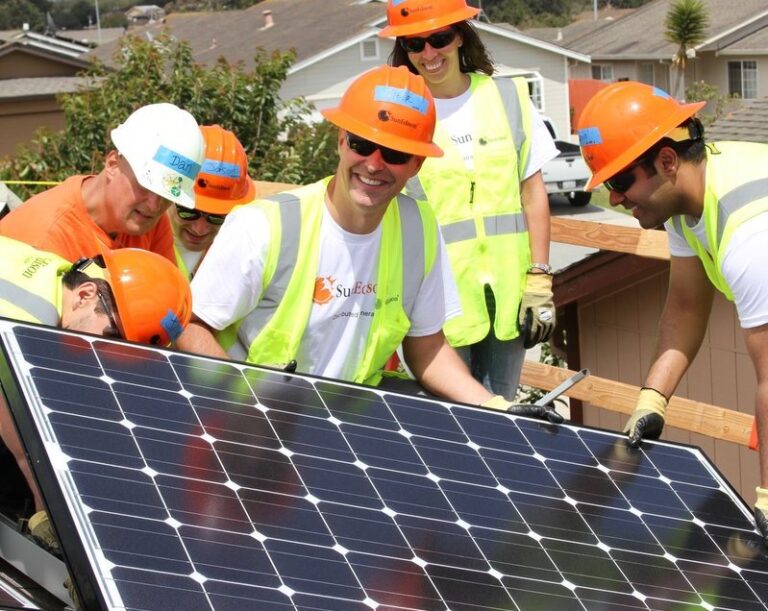 Four workers in safety gear installing a solar panel on a residential roof