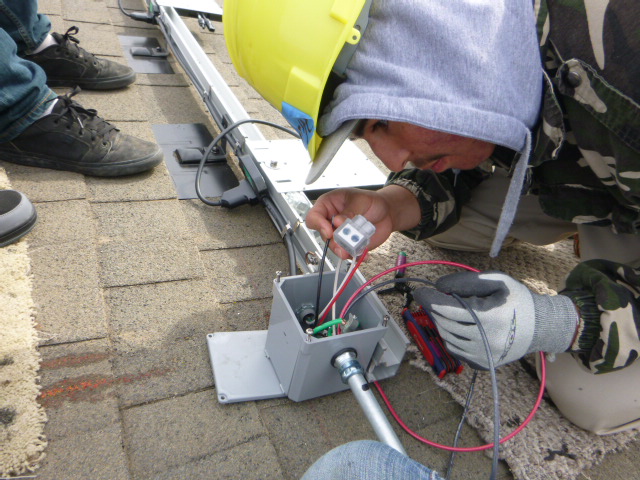 Person in safety gear connecting colored wires to electrical equipment outdoors during construction or maintenance work