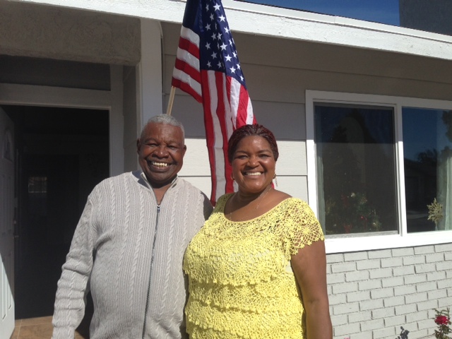 Two people smiling in front of a building with an American flag