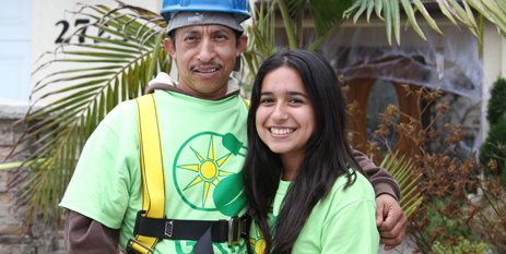 Two volunteers in green shirts and safety gear smile at a solar energy event