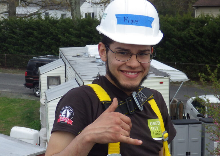 Miguel wearing safety gear and hard hat gives thumbs up at construction site
