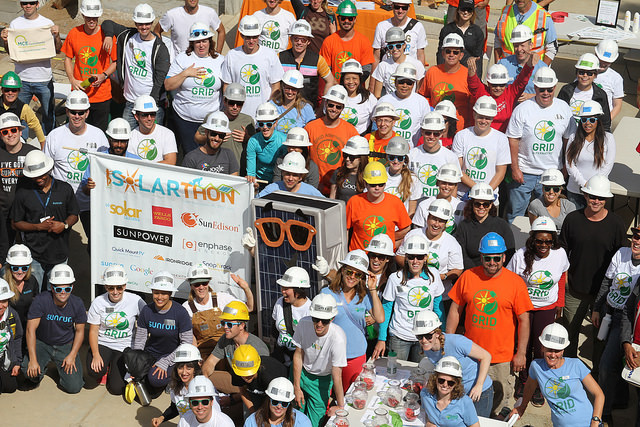 Large group of GRID Bay Area volunteers in hard hats and orange shirts holding a Solarathon banner at a community event
