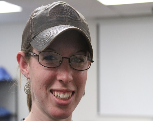 Smiling person wearing glasses and a gray baseball cap indoors