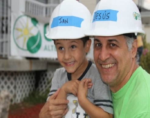 Man and boy wearing white hard hats labeled "San" and "Jesus" at a construction site