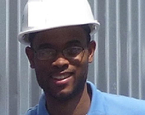 Man wearing white hard hat and blue shirt smiling at camera