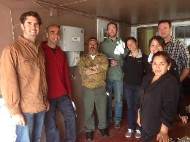 Group of eight people posing together indoors in front of a water heater