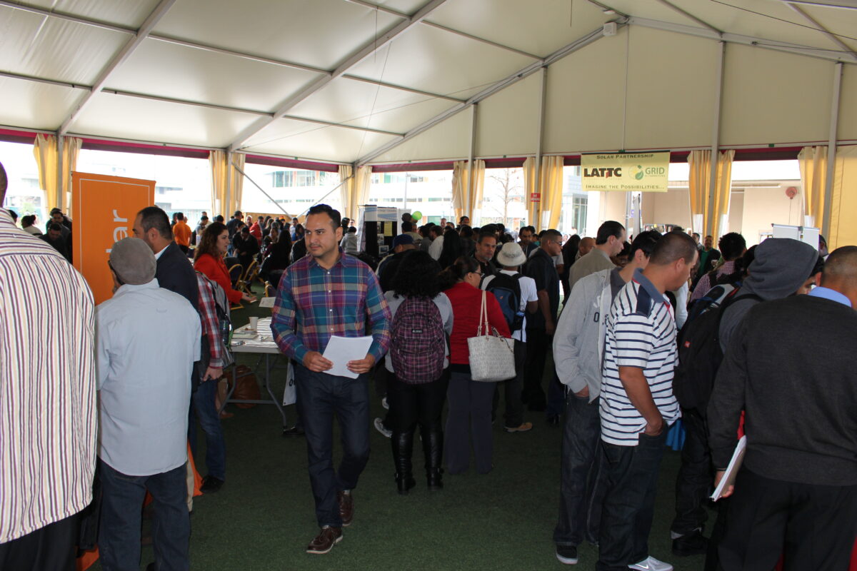 Large crowd gathered in tent venue with yellow curtains and signage, attending a job fair or event about solar energy careers