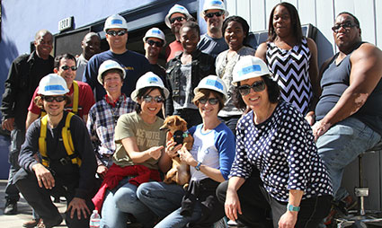Group of diverse workers and community members wearing hard hats and safety gear posing together at a construction or industrial site