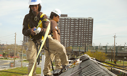 Two workers installing solar panels on a residential building roof in an urban area