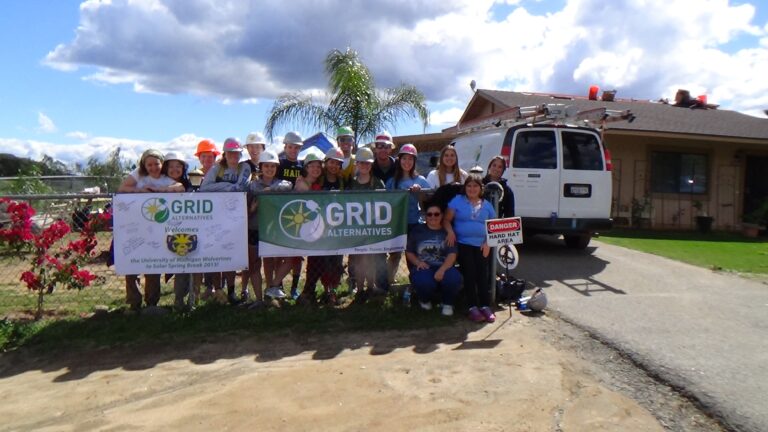 Group holding GRID Alternatives banners at solar installation project site with house and van visible
