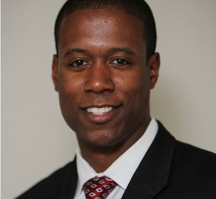 Professional headshot of a smiling man in business attire with burgundy tie