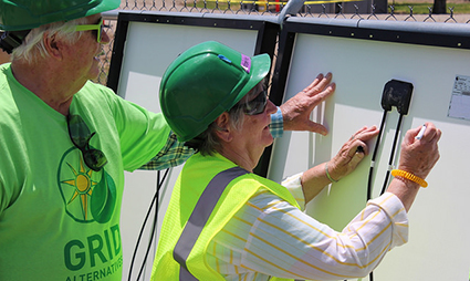 Construction workers in safety gear installing community solar panels on a roof