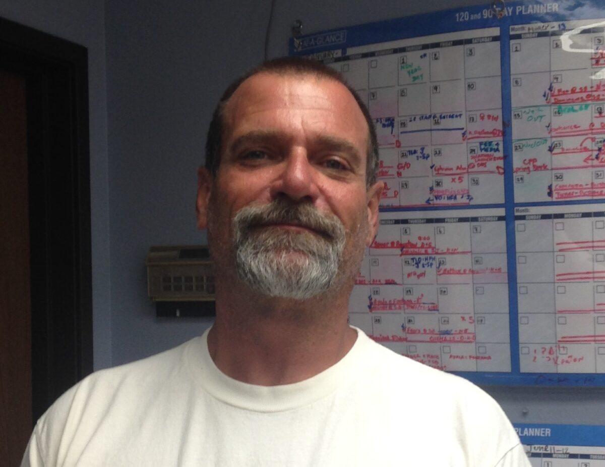 Man in white shirt standing in front of a blue day planner with handwritten notes and markings