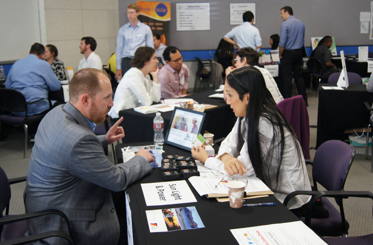 Professional networking event at solar jobs fair with attendees in business attire discussing career opportunities at tables