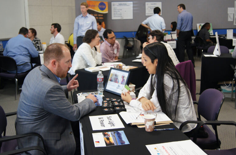Professional networking event at solar jobs fair with attendees in business attire discussing career opportunities at tables