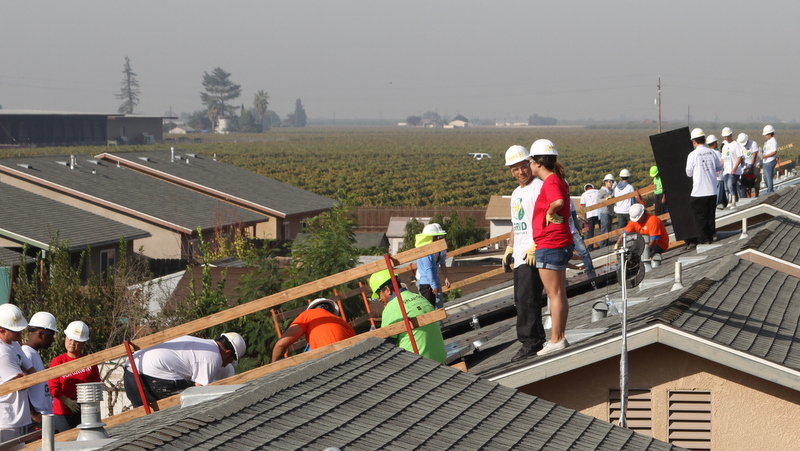Construction workers in hard hats on residential roofing project with agricultural fields visible in background