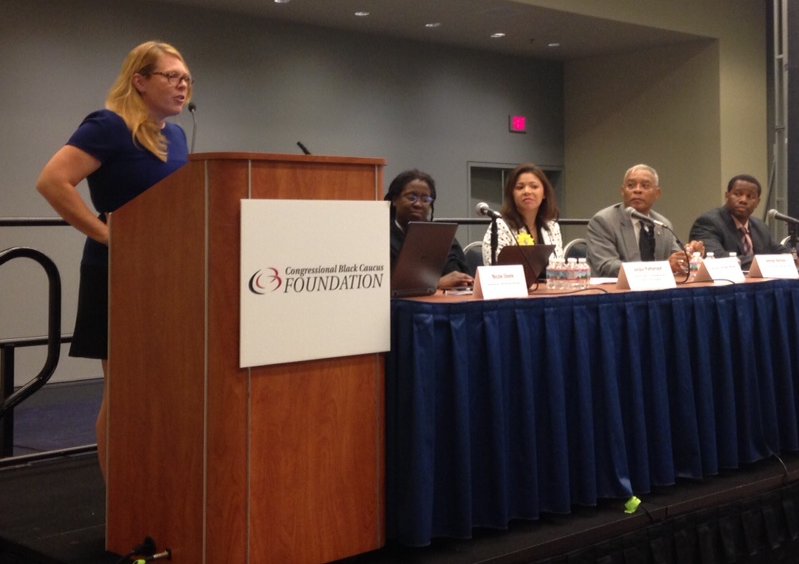 Woman speaking at podium with Congressional Black Caucus Foundation logo, four panelists seated behind blue-draped table