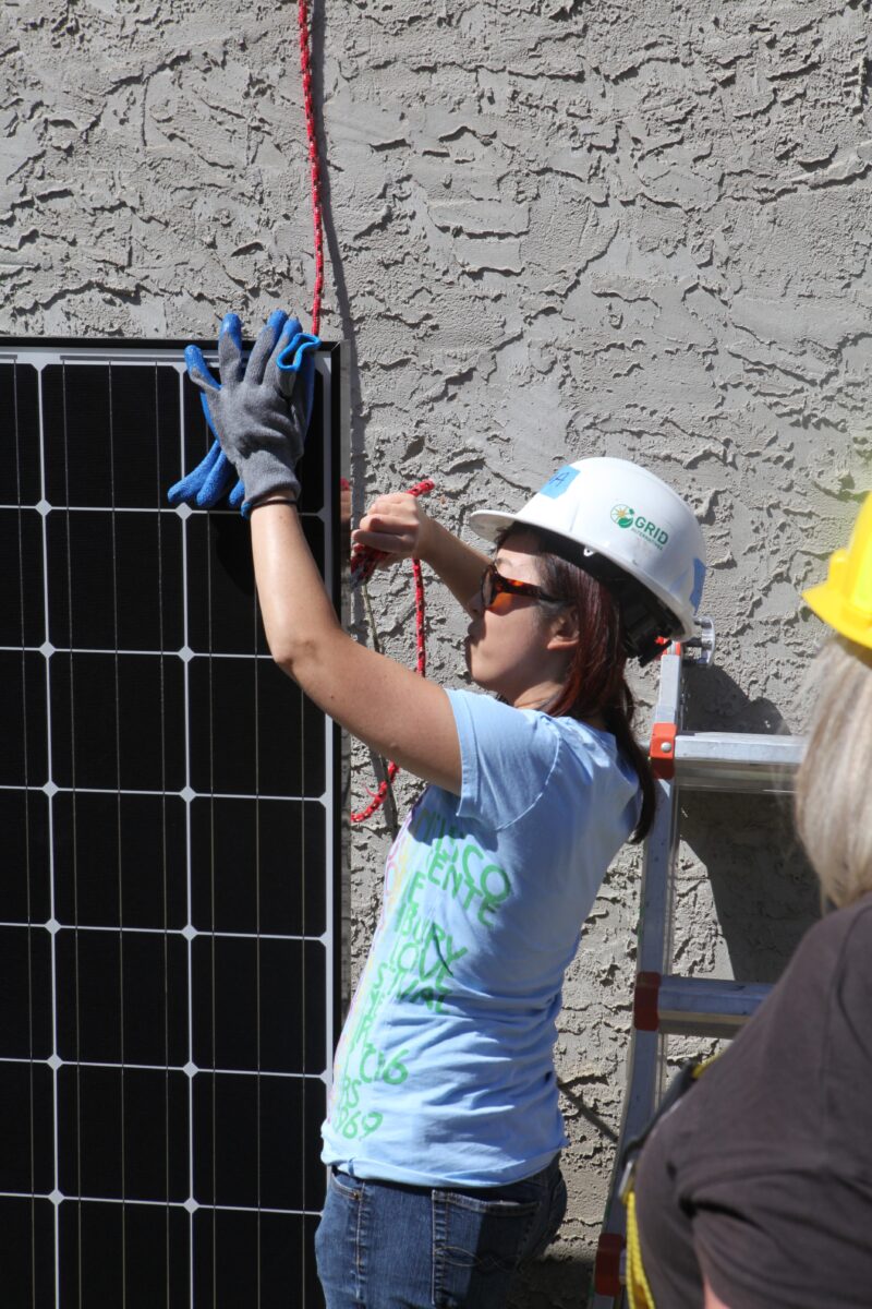 Worker in safety gear installing solar panel on concrete wall during community solar project