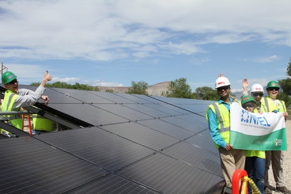 Workers in safety gear installing solar panels on rooftop with NREL banner