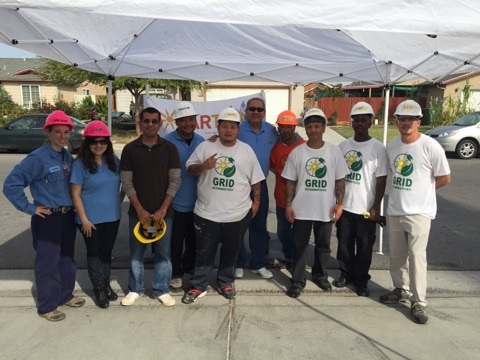 Group of people wearing hard hats and GRID t-shirts standing under a tent at a solar job fair event