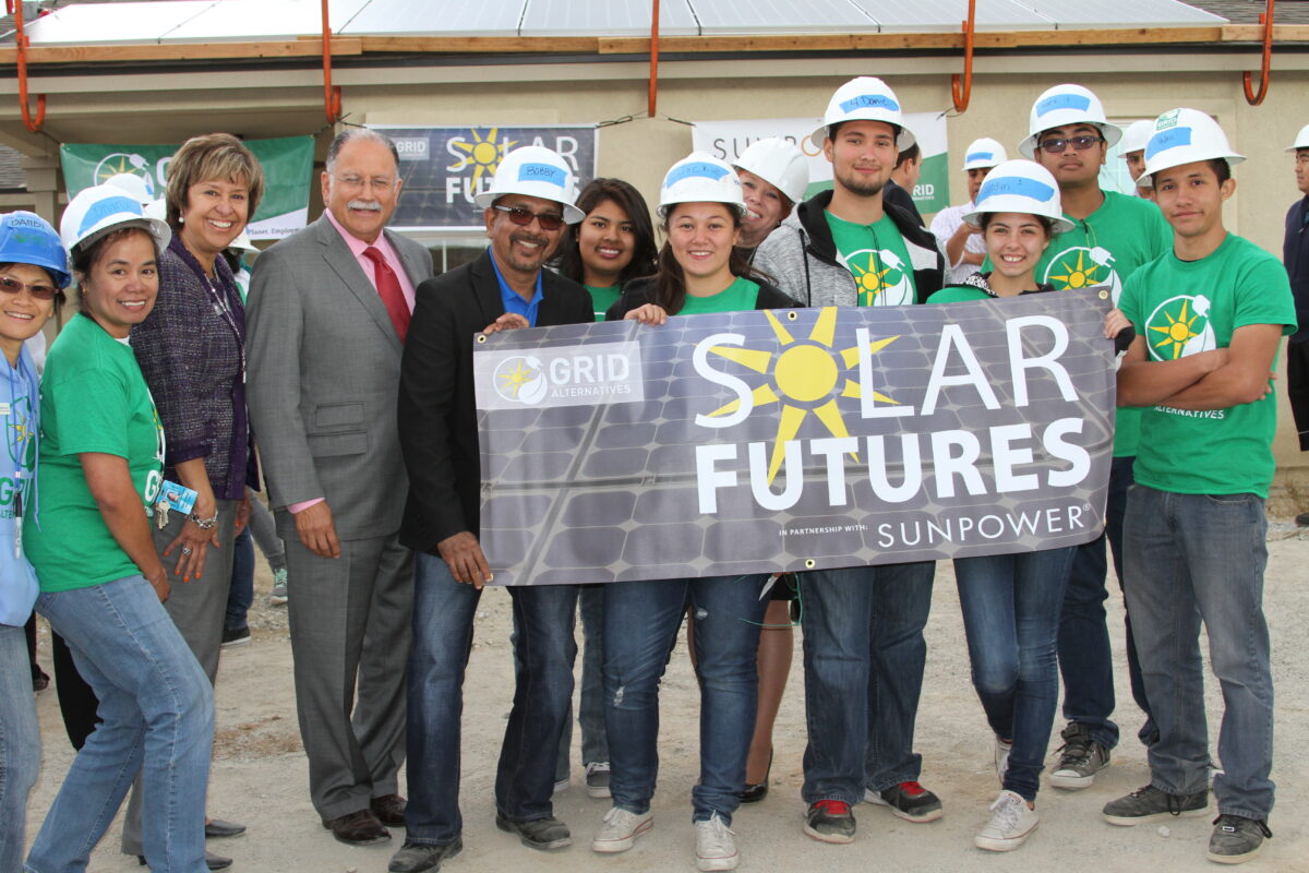 Group of students and officials holding a "Solar Futures" banner with Sunpower logo at a solar installation site